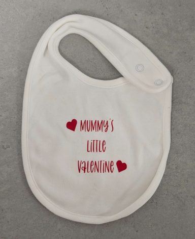 Baby Bib White bib with "Mummy’s Little Valentine" printed in red text surrounded by red hearts.