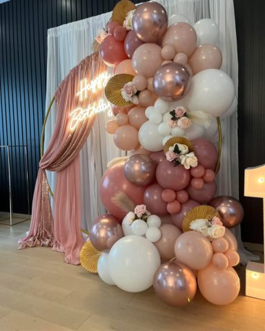 2m Hoop with Garland Colourful balloon display with floral accents and a pink curtain backdrop.