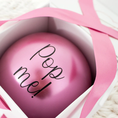 Balloon in a Box Pink balloon with "Pop me!" written on it, placed inside a box with pink ribbon.